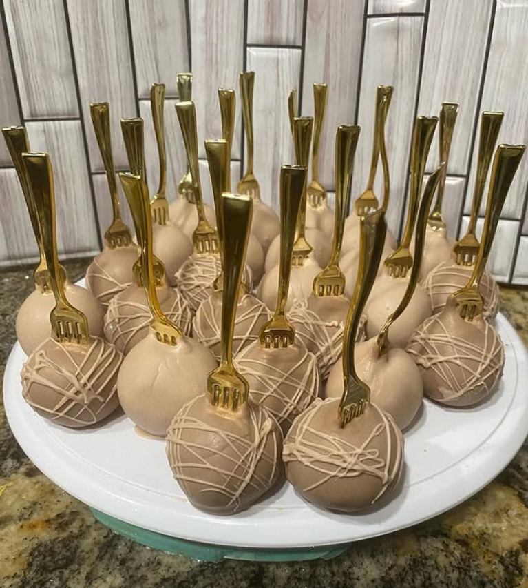 Plate of chocolate-coated cake balls with a light drizzle, each speared with a small gold fork.