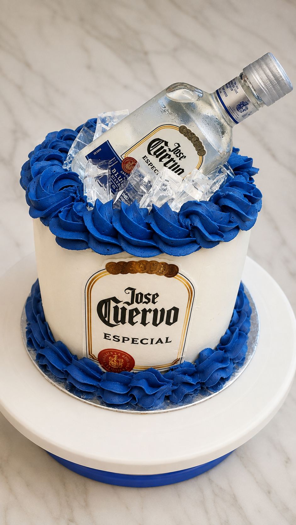 White cake with cobalt blue buttercream rosettes, a tequila bottle resting in clear ice on top, and a matching printed label on the side.